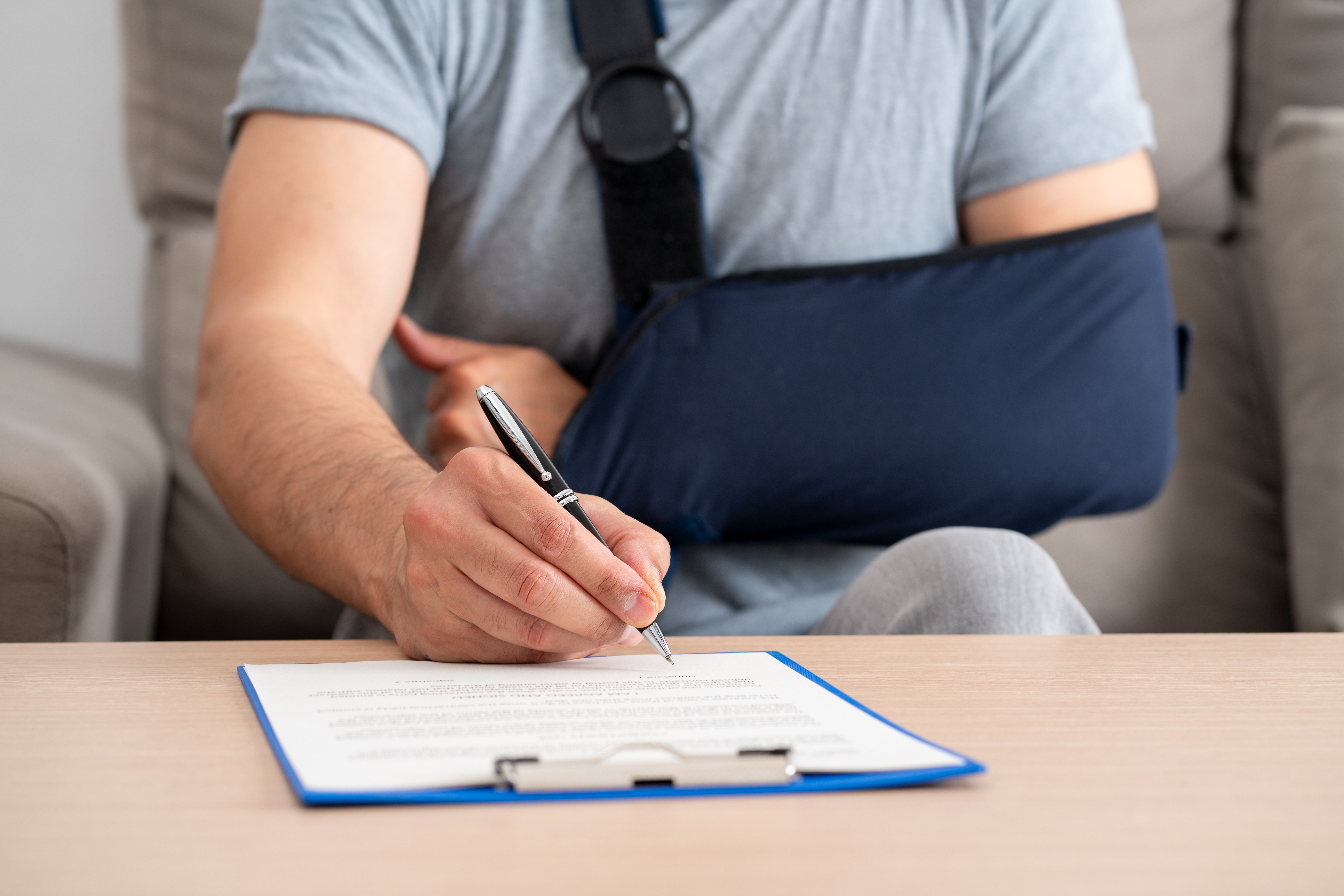 man with broken arm sits at table signing contract - insurance tactics in KS and MO personal injury claims