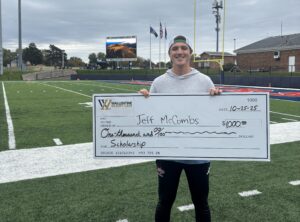 young man poses with giant scholarship check on football field - Wallentine Injury Law 2025 Community Involvement Report