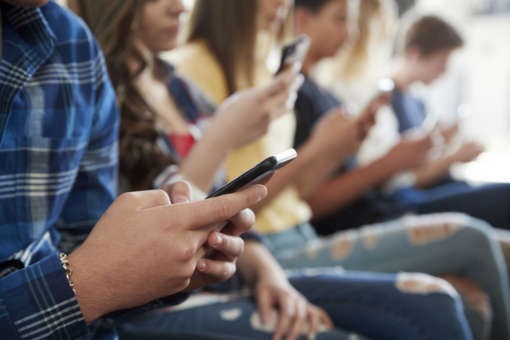 teenagers sit in line scrolling on their phones - Missouri social media harm lawyers